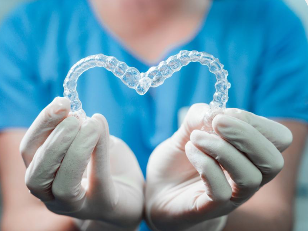 Gloved hands holding two clear aligners arranged in a heart shape