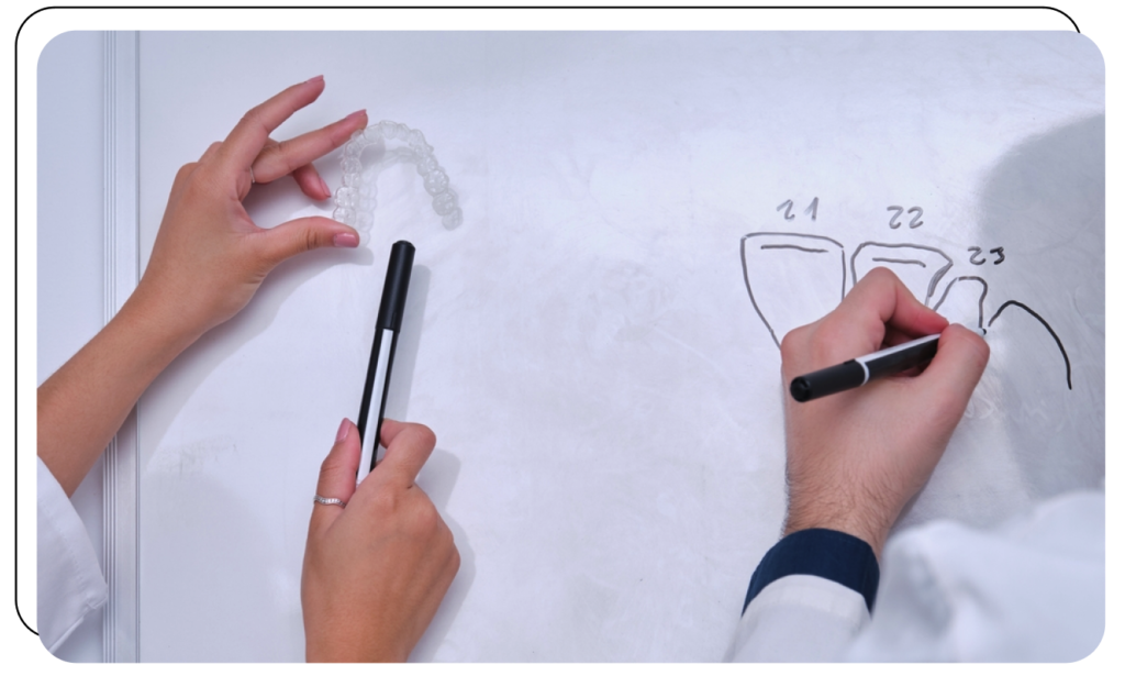 Two clinicians sketching tooth diagrams on a whiteboard beside a clear aligner